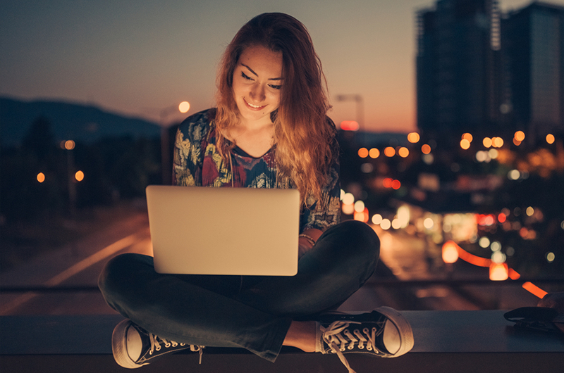 Woman with laptop sitting cross-legged on balcony