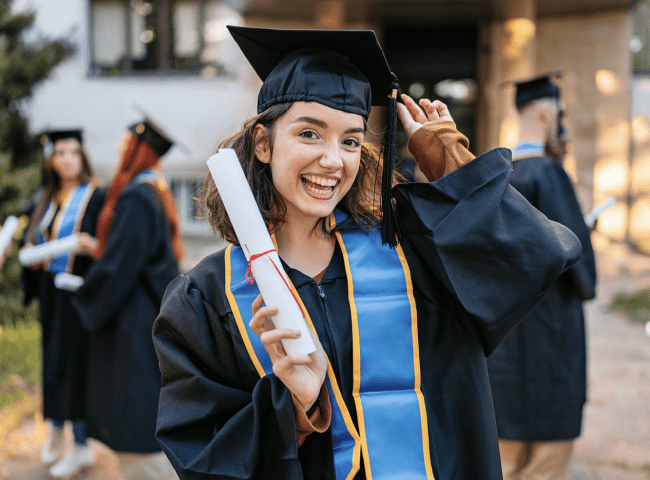 A young woman in a graduation cap and gown smiling